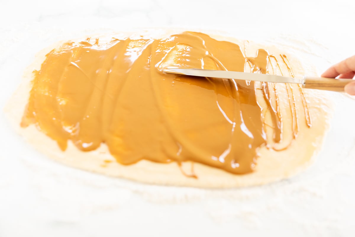 A person is using a knife to spread caramel on Cookie Butter Cinnamon Rolls.