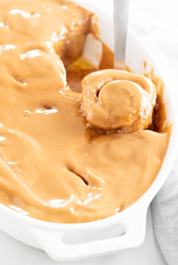 A person scooping cookie butter cinnamon rolls from a white dish.