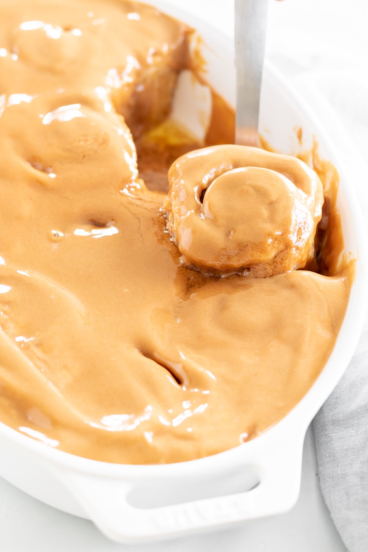 A person scooping cookie butter cinnamon rolls from a white dish.