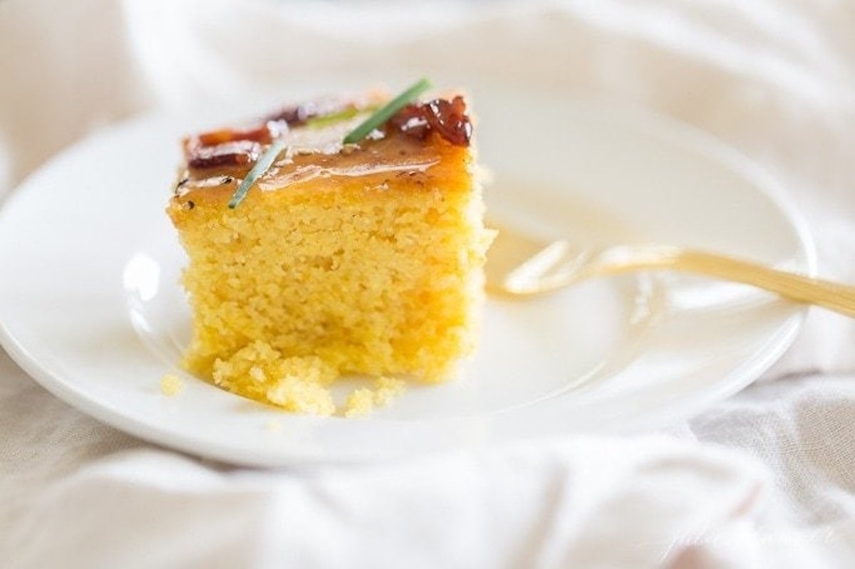A piece of yellow cake on a plate with a gold fork.