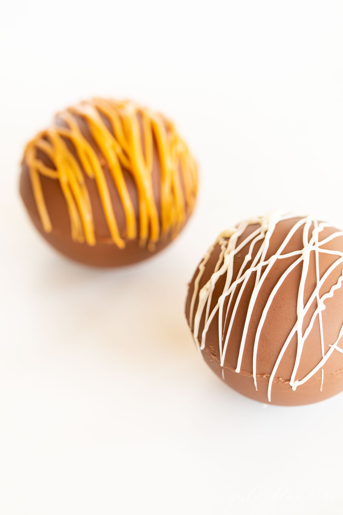 Two hot chocolate bombs on a white surface.