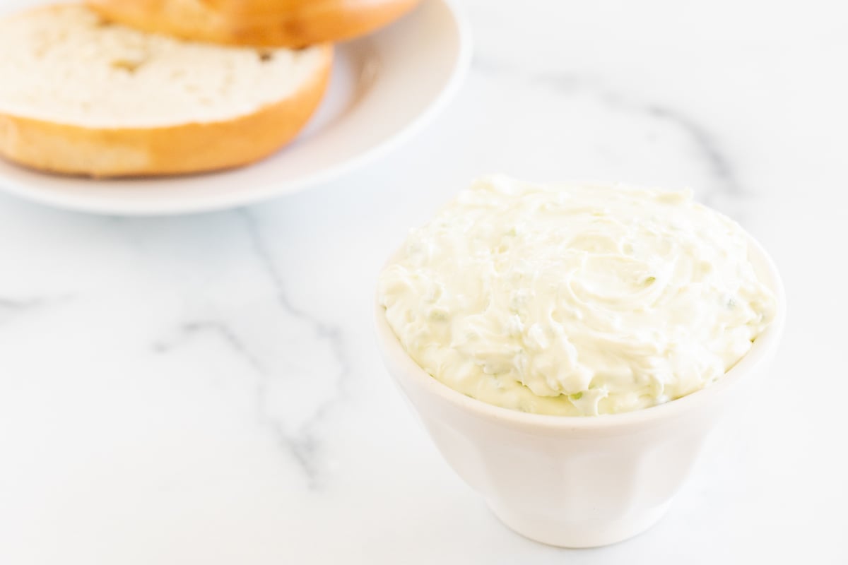 A bowl of jalapeño cream cheese and a bagel on a table.