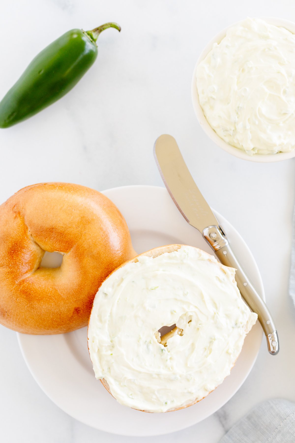 A delicious bagel topped with cream cheese and a jalapeno, served on a plate.