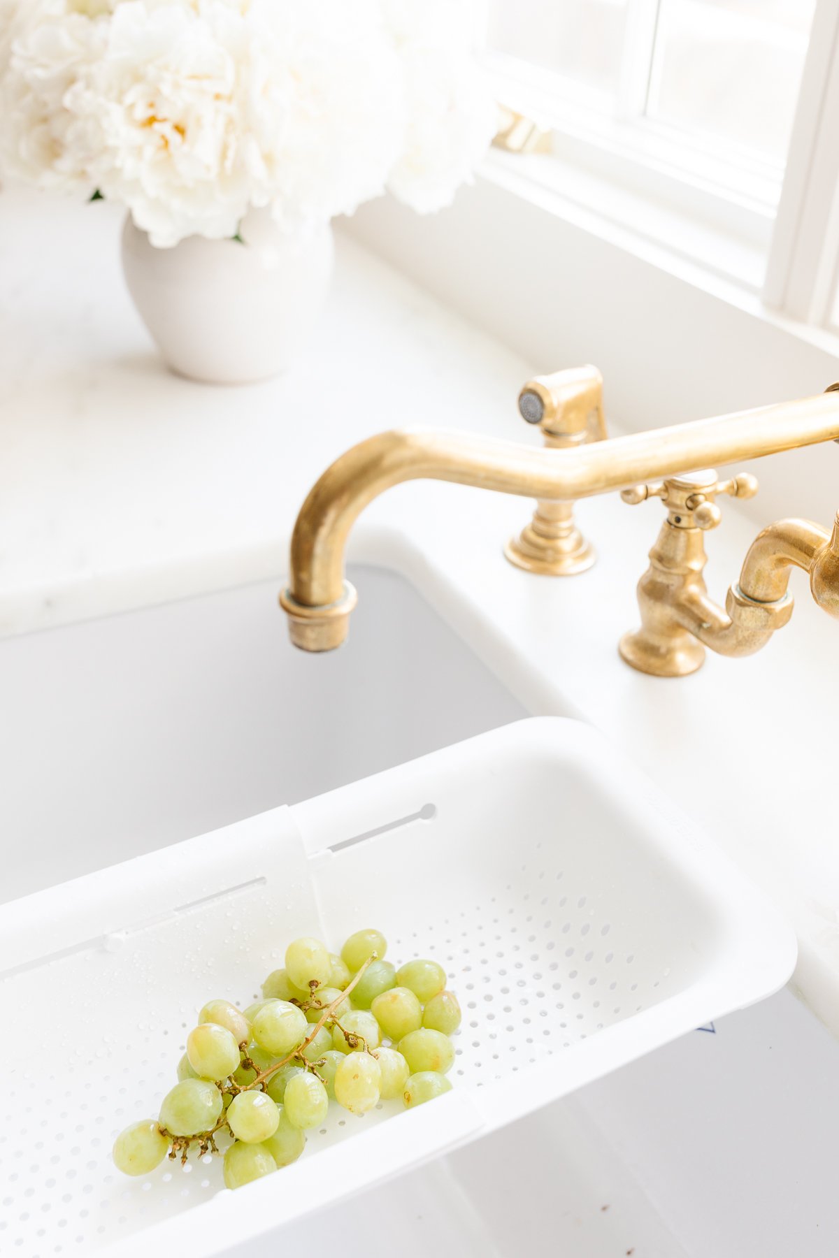 A kitchen sink adorned with unlacquered brass faucets, complemented by clusters of grapes immersed in water.