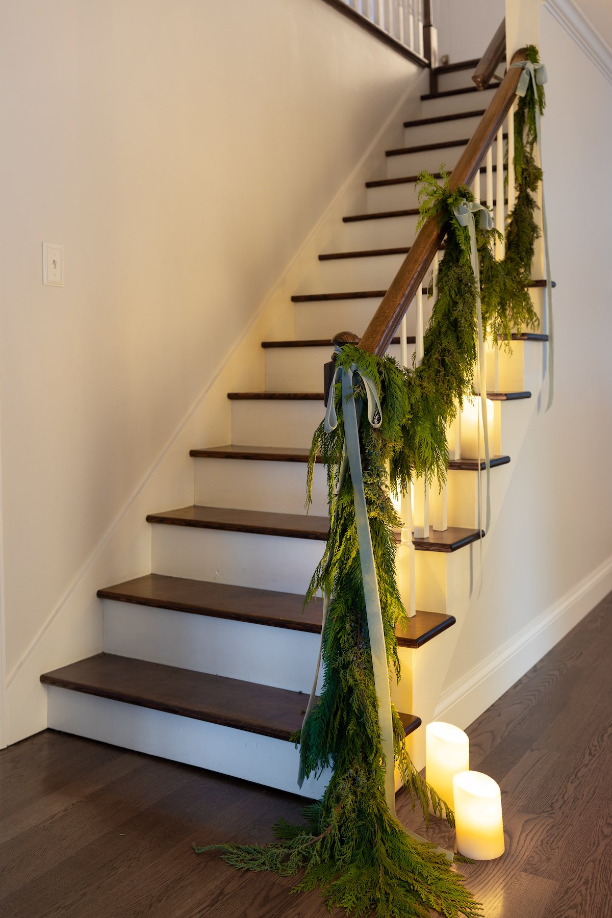 A christmas garland on a staircase decorated with LED pillar candles.