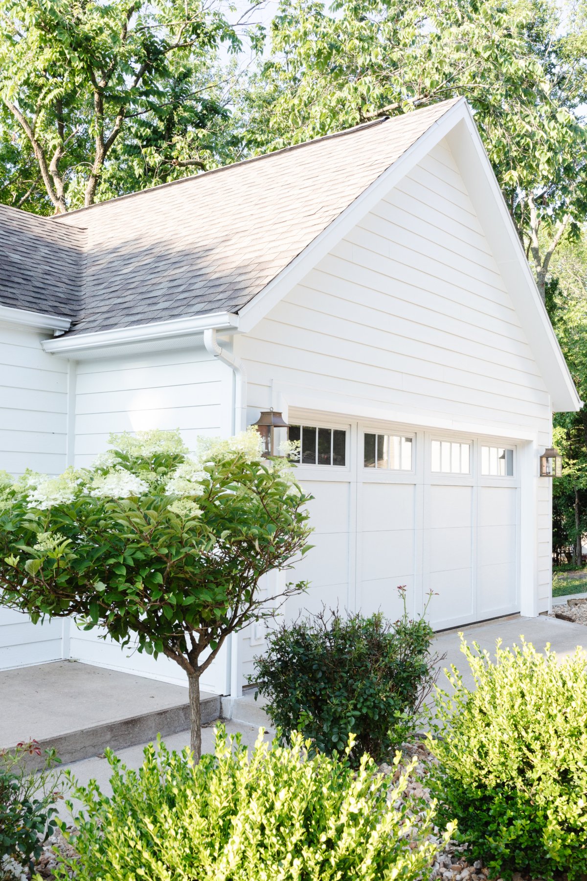 A white garage with bushes and shrubs.