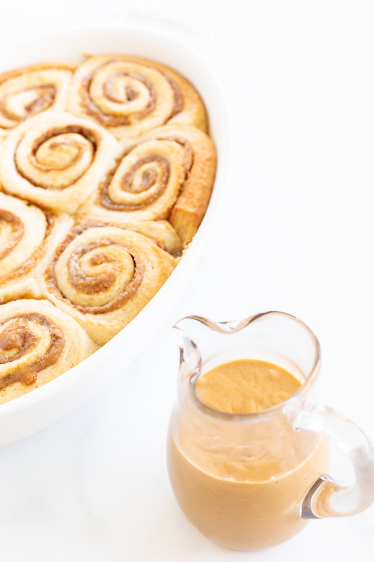 A white dish with cinnamon rolls and a clear glass container of Biscoff frosting