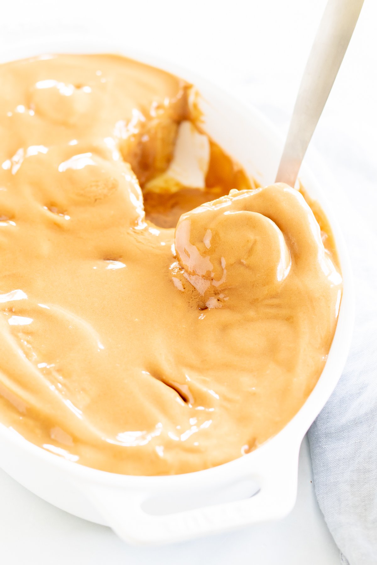 A person scooping a biscoff cinnamon roll covering in cookie butter icing, from a pan.