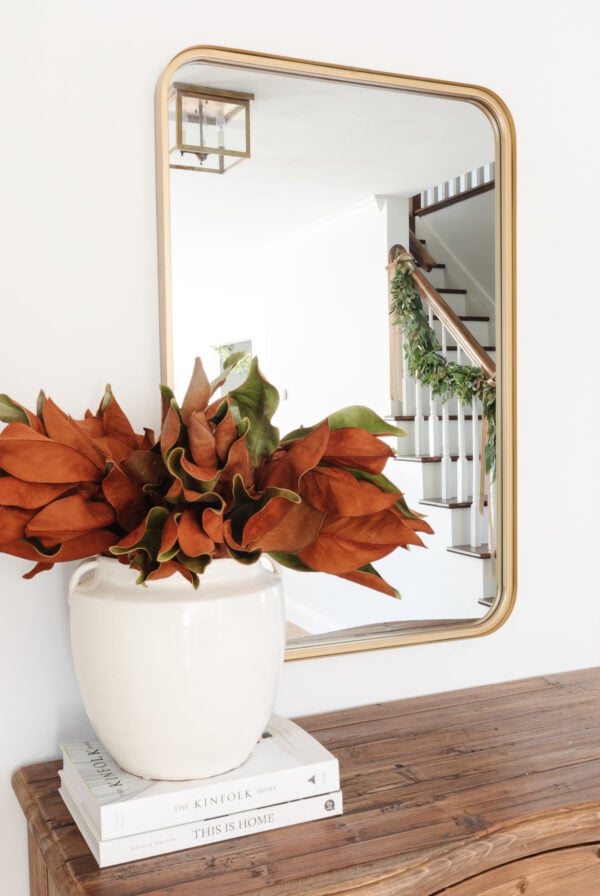 A vase of faux flowers on a table next to a mirror.