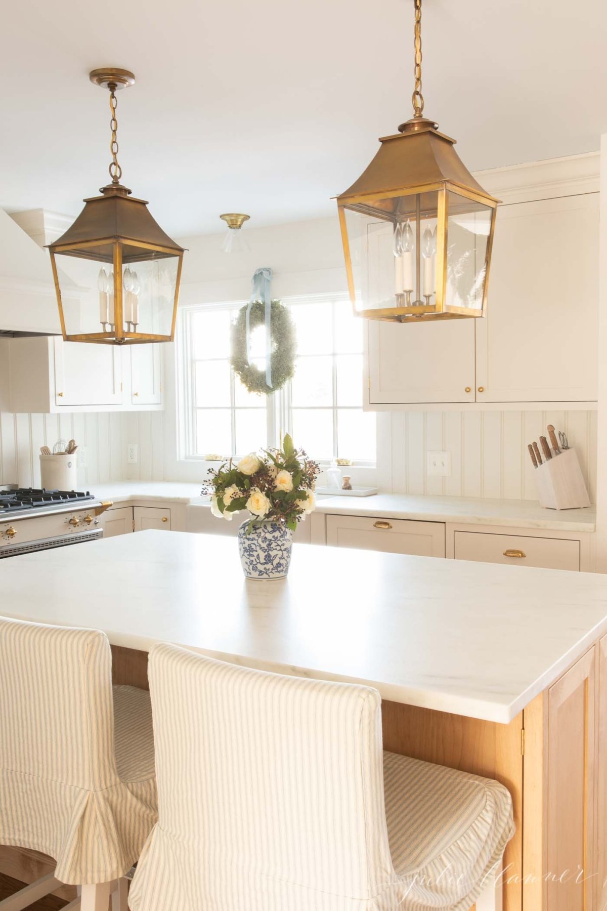 A white kitchen with a white island and brass lanterns.