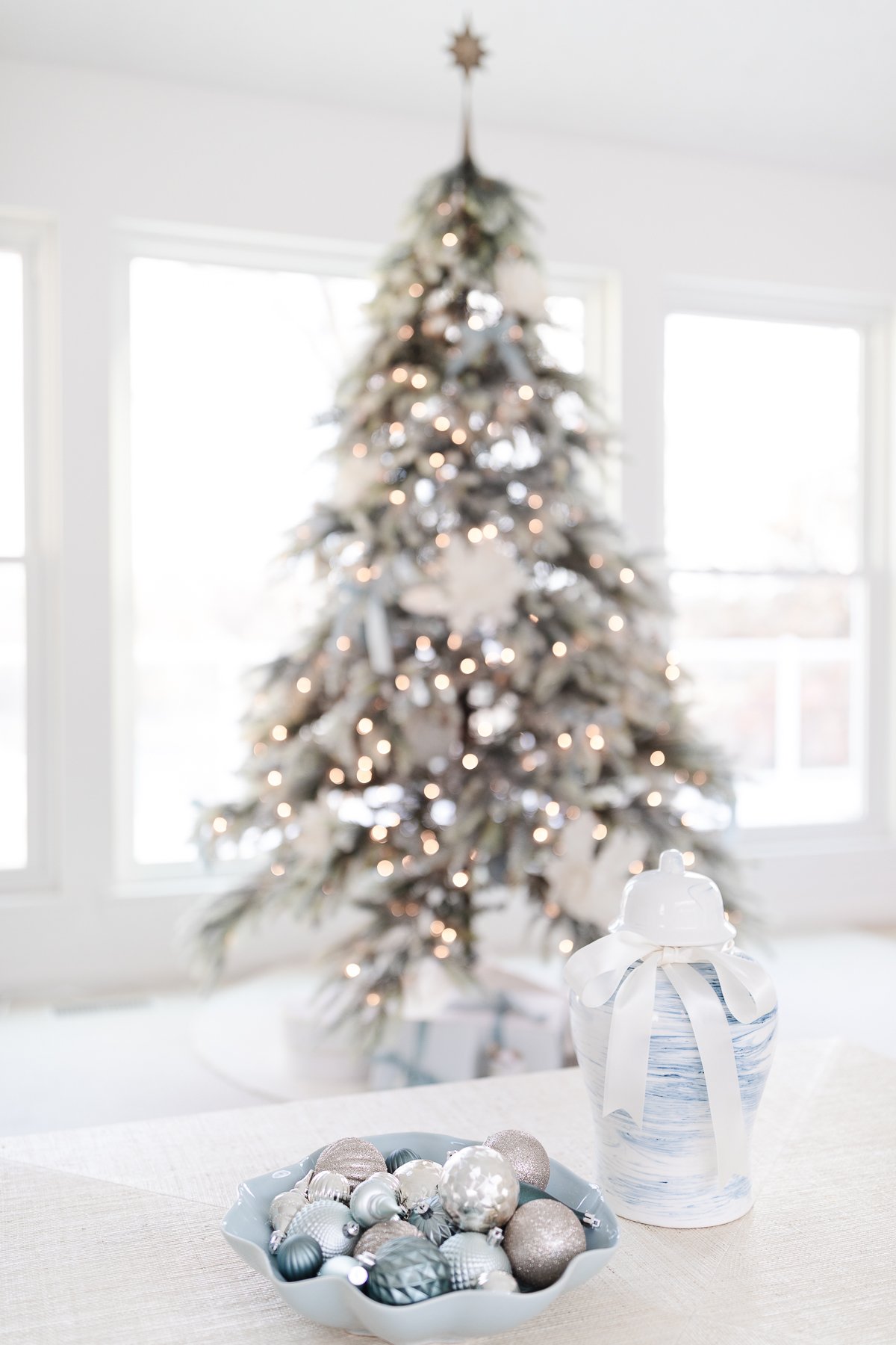 A christmas tree with ornaments on a table in front of a window.