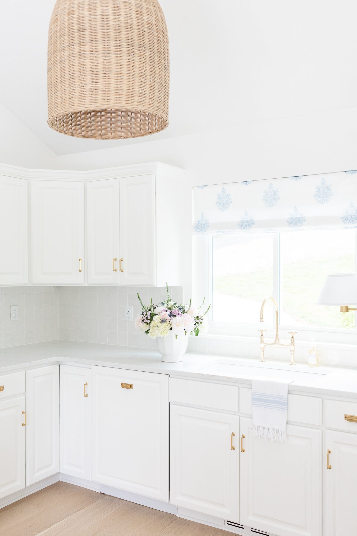 A white kitchen with a wicker pendant light, featuring kitchen counter organization.