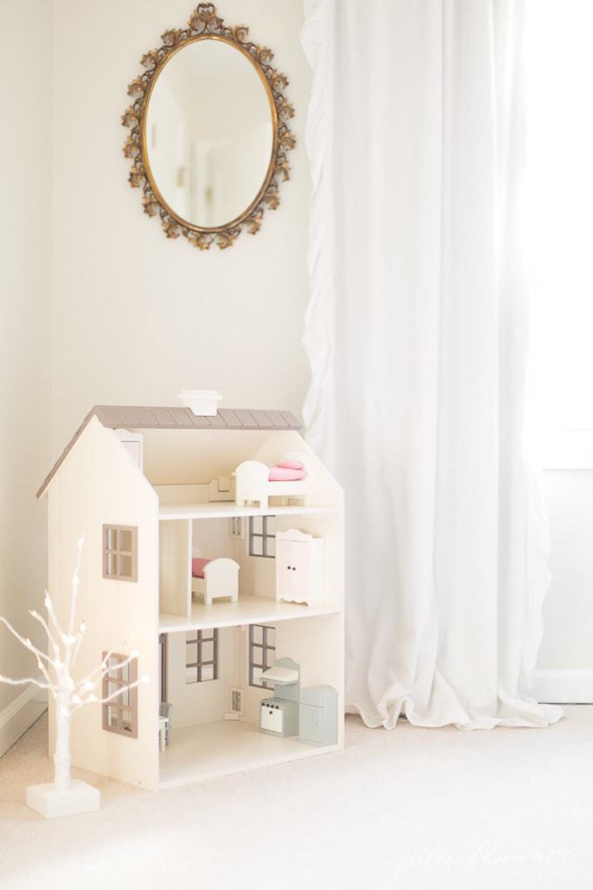 Experience the enchanting Christmas magic of a doll house nestled in a white room, adorned with a mirror.
