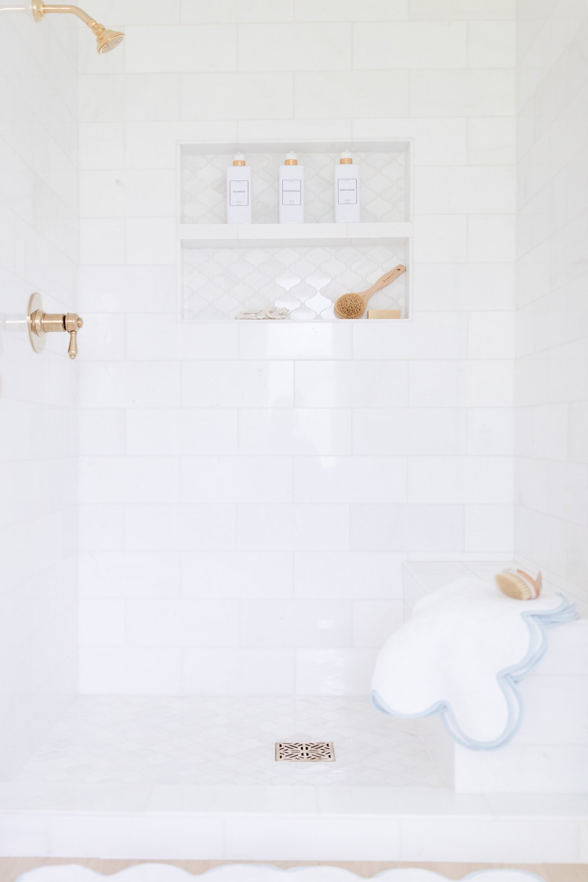 A white tiled shower with a blue and white rug.