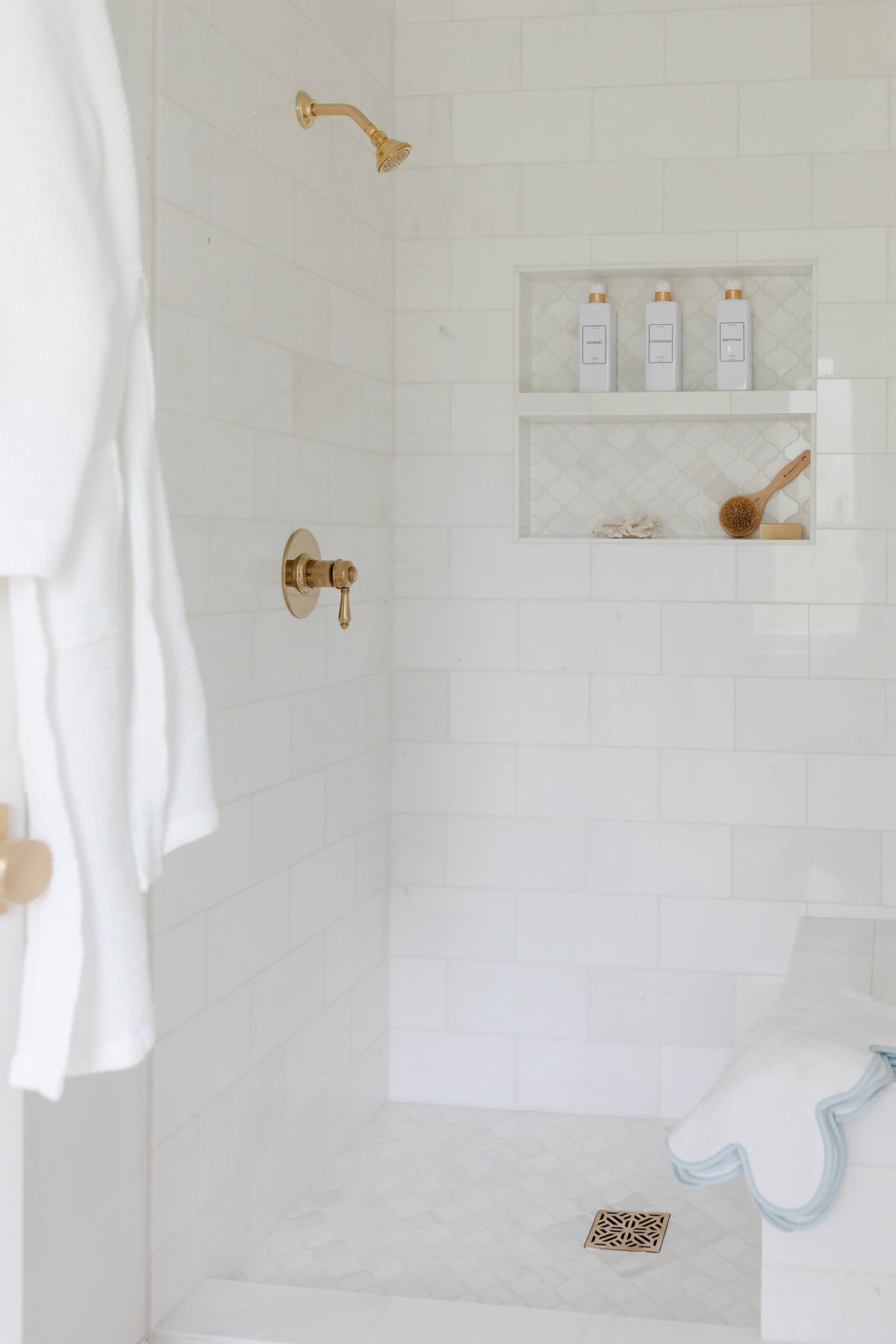 A white tiled shower with a towel hanging on the wall.