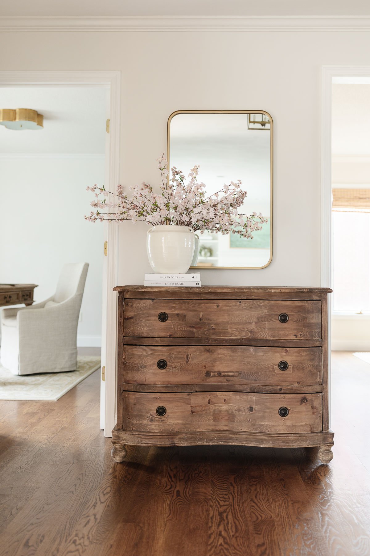 A curved wooden dresser in a room with a mirror.