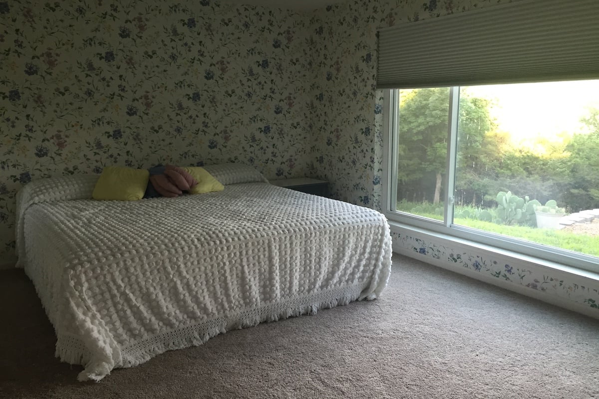 A bedroom with floral wallpaper and a window, showcasing the charm of dated wallpaper.