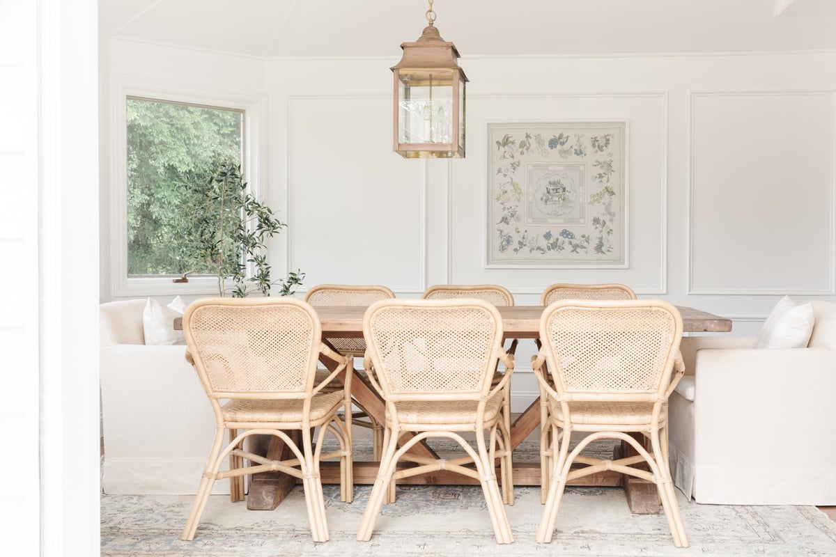 This dining room features wicker chairs and a stunning chandelier, with an indoor olive tree adding a touch of natural elegance.