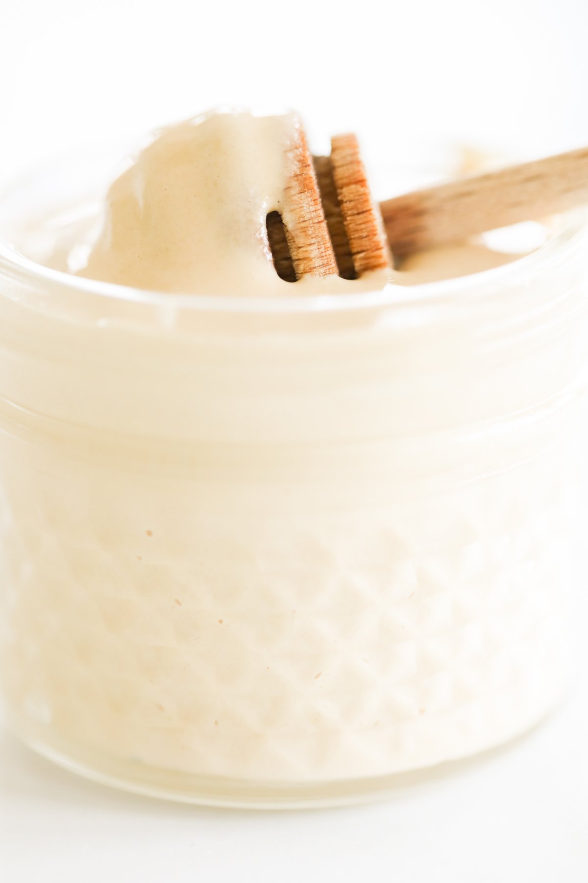 A wooden spoon is pulling whipped honey out of a jar.