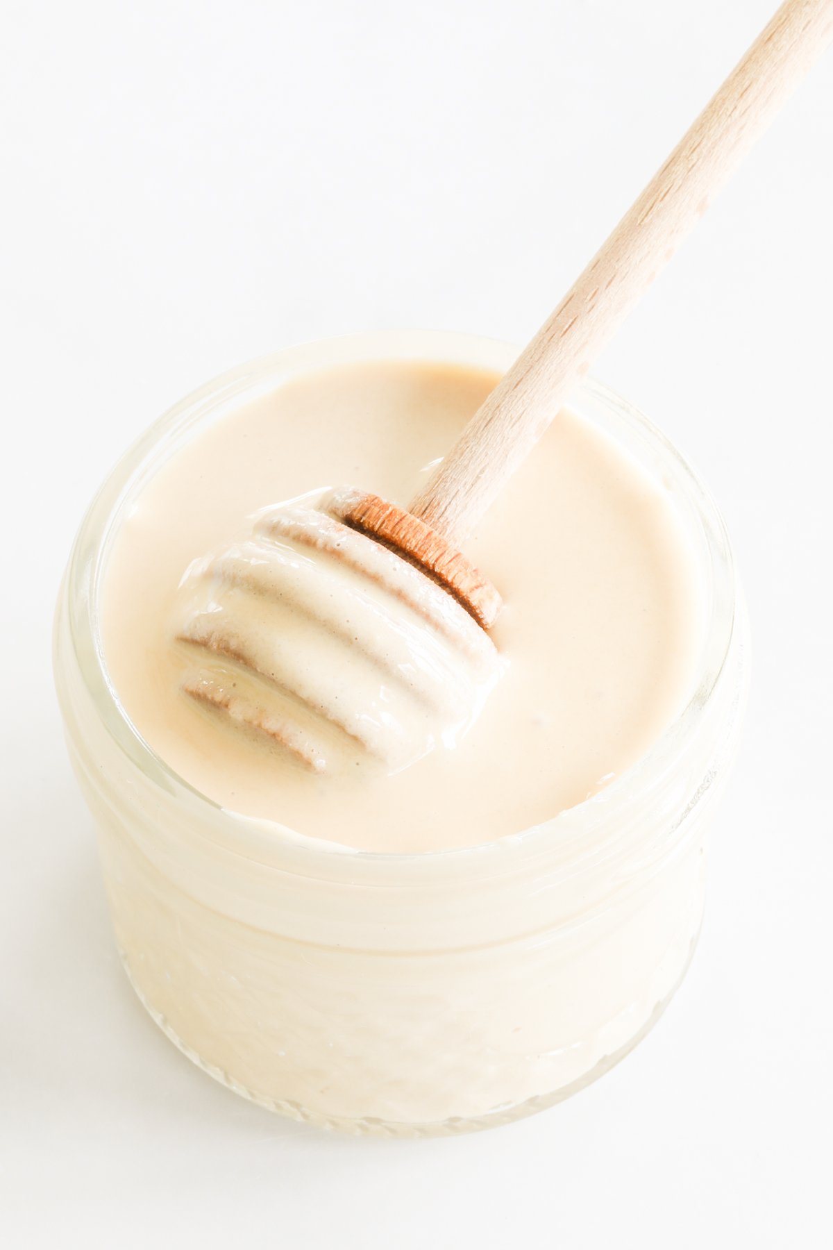 A wooden spoon is pulling whipped honey out of a jar.