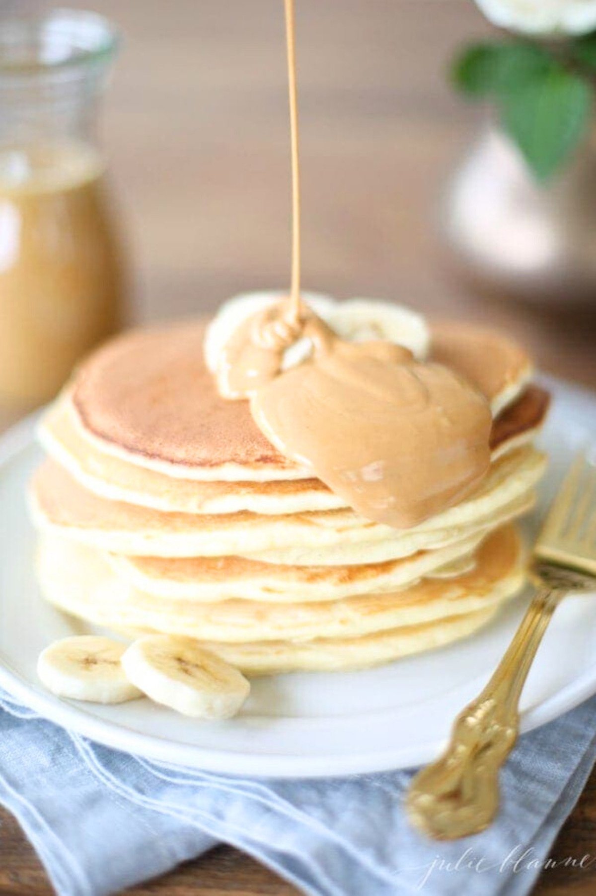 A classic stack of pancakes is being drizzled with peanut butter.