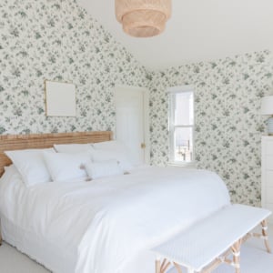 A white bed in a bedroom with floral wallpaper.