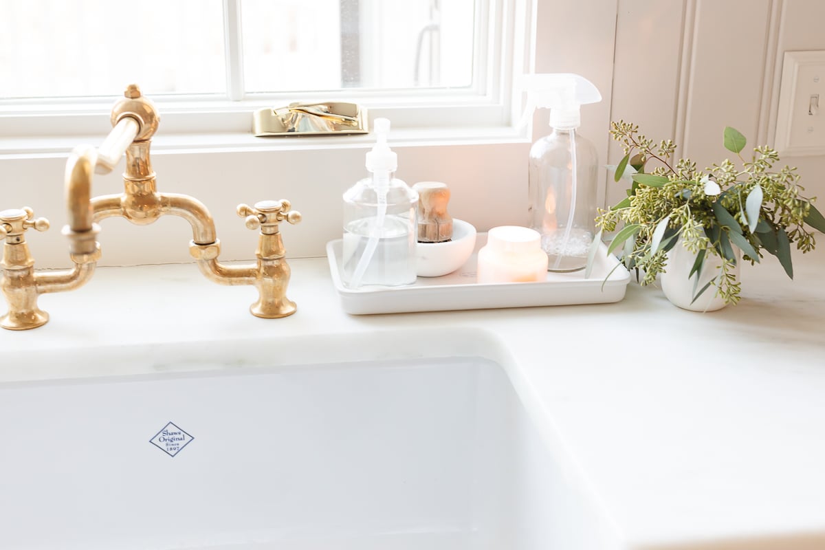 Discover elegant and functional under sink storage ideas for a white kitchen sink with a gold faucet.