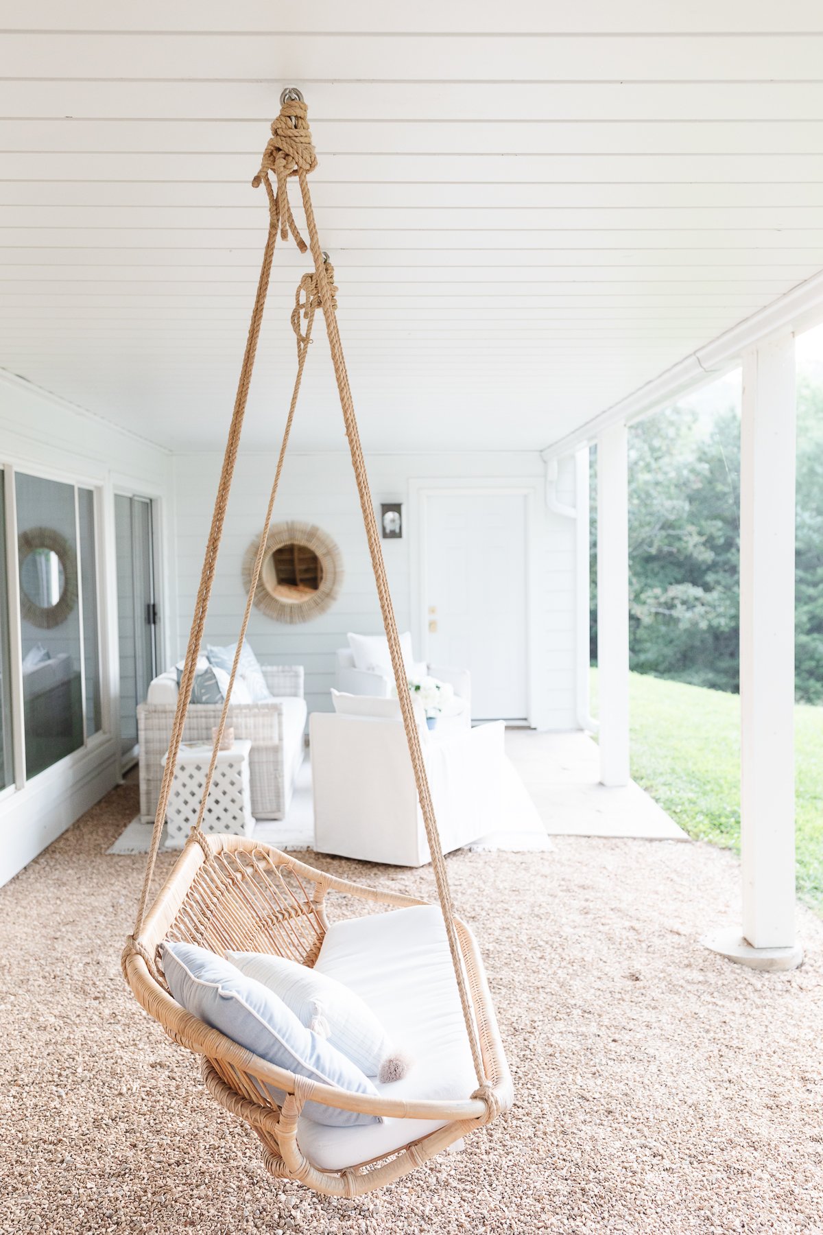 A wicker swing hanging from a porch at a lake house.