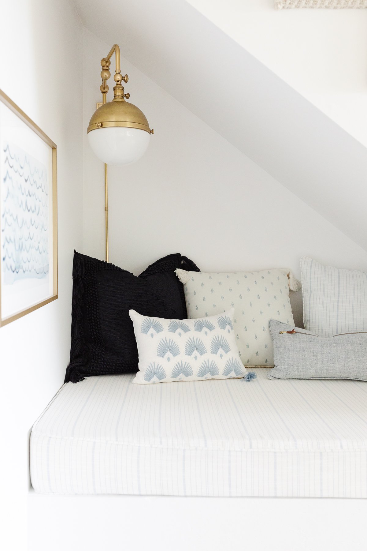 A bed under the stairs with pillows and a lamp.