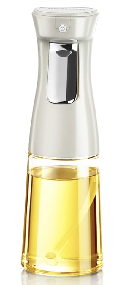 A clear oil dispenser bottle, a must-have among kitchen gadgets, features a white spray top and metallic trigger. Filled with yellow liquid, it stands upright against a plain white background.