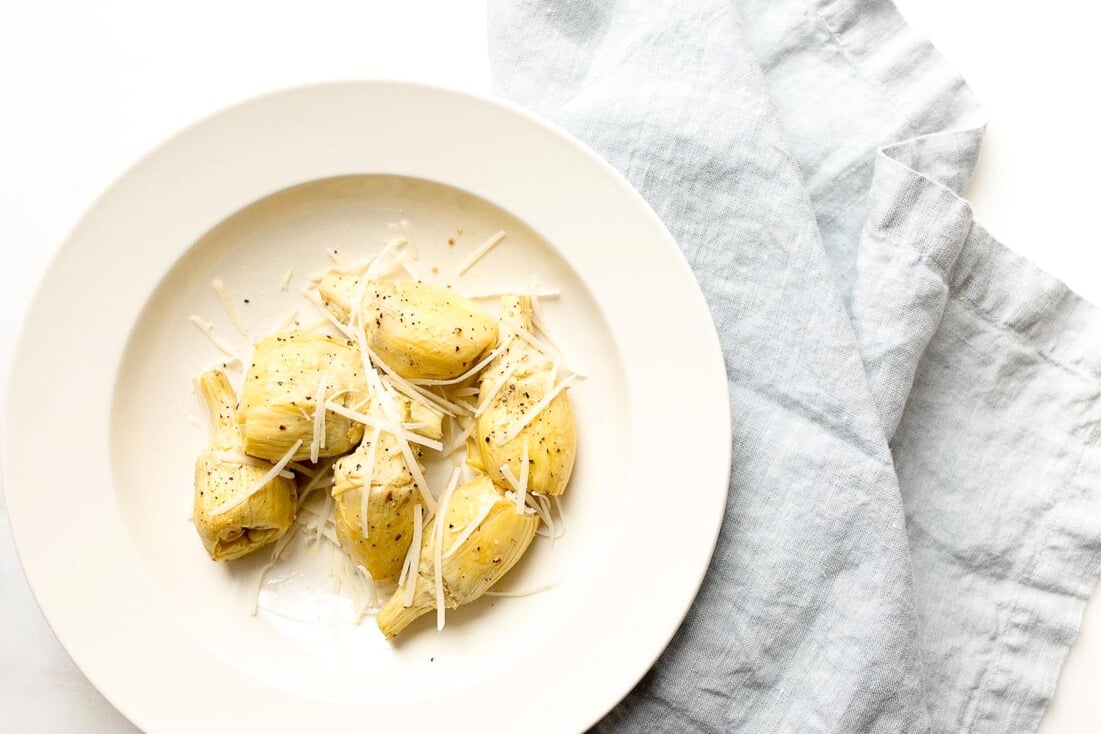 baked artichoke garnished with parmesan in cream serving bowl