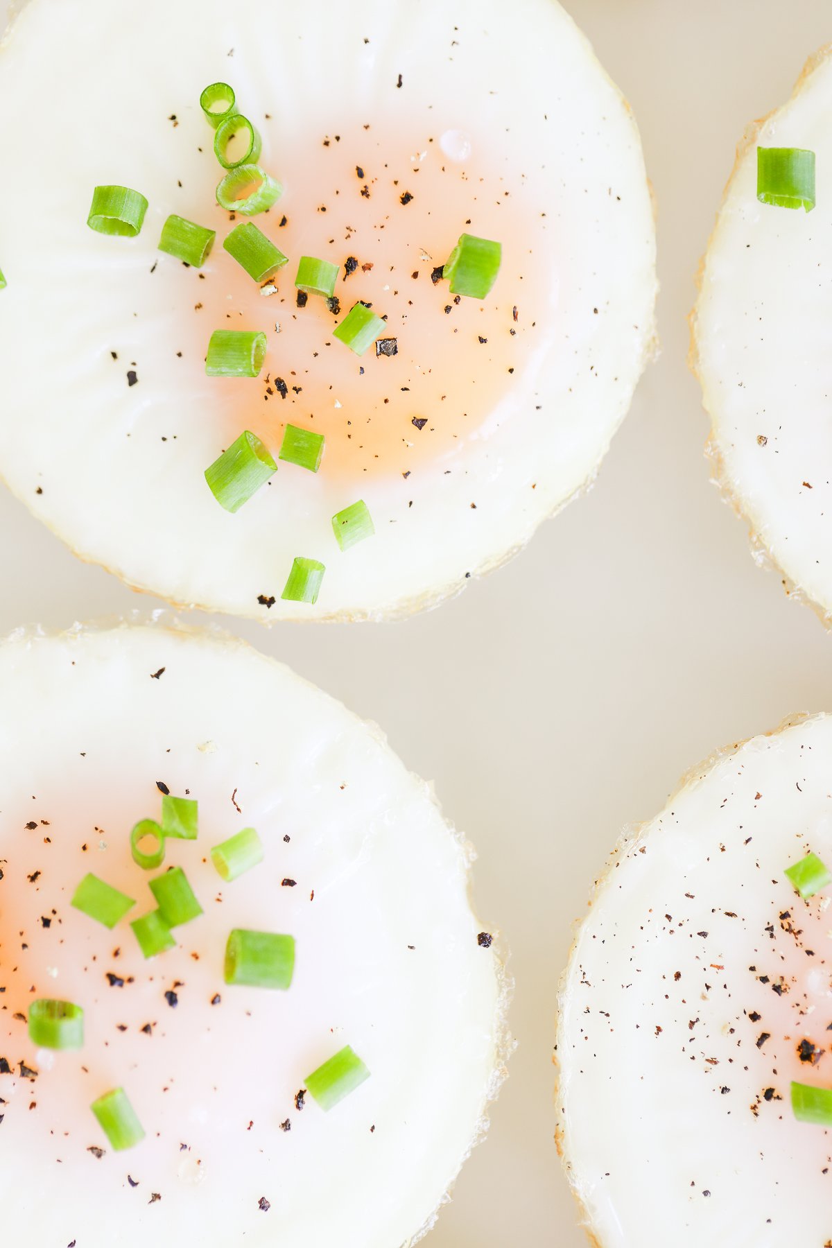 A plate of sunny side up baked muffin pan eggs garnished with herbs, pepper, and salt.