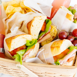 A picnic basket filled with sandwiches, chips, grapes, and a bottle of beverage, offering some of the best picnic food ideas.