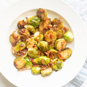 Crispy brussel sprouts on a white plate with a blue linen napkin and serving spoon to the side.