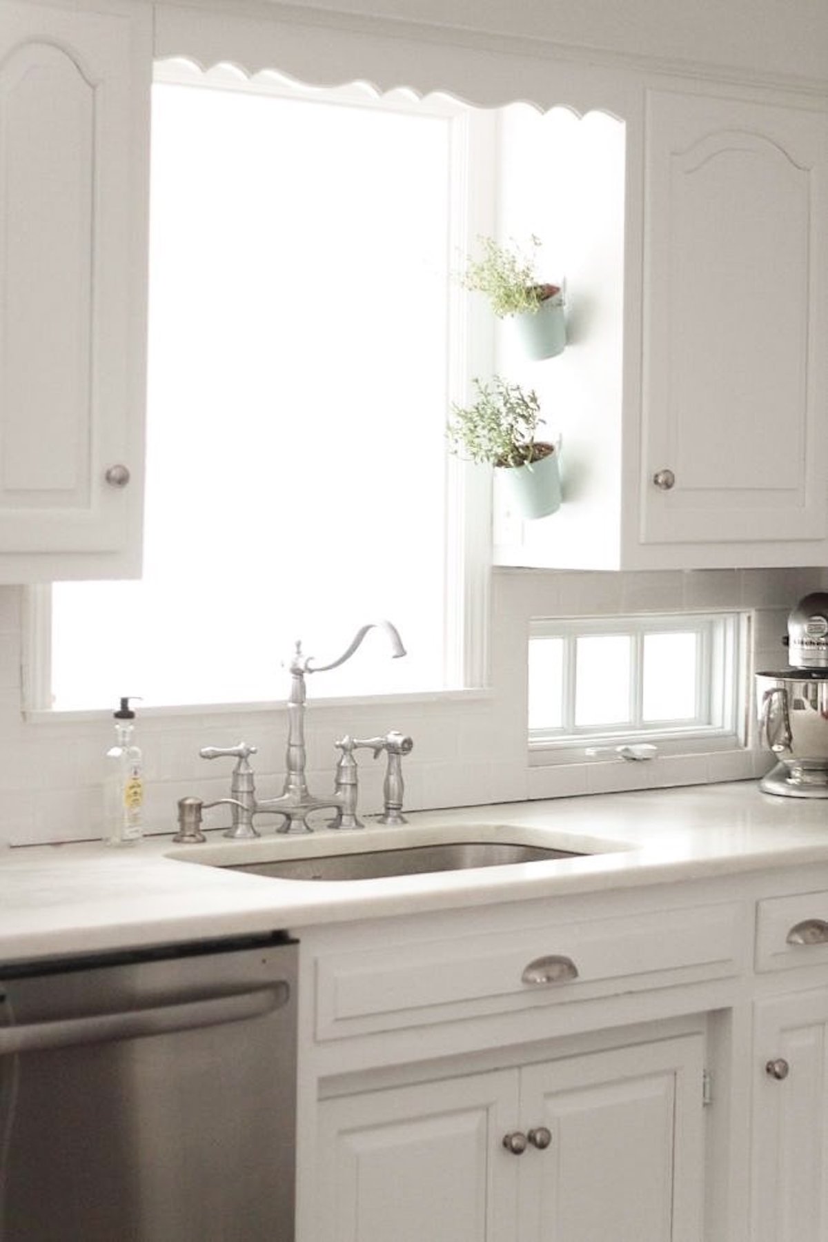A white kitchen with pots hanging alongside the cabinets for an indoor vertical garden. 
