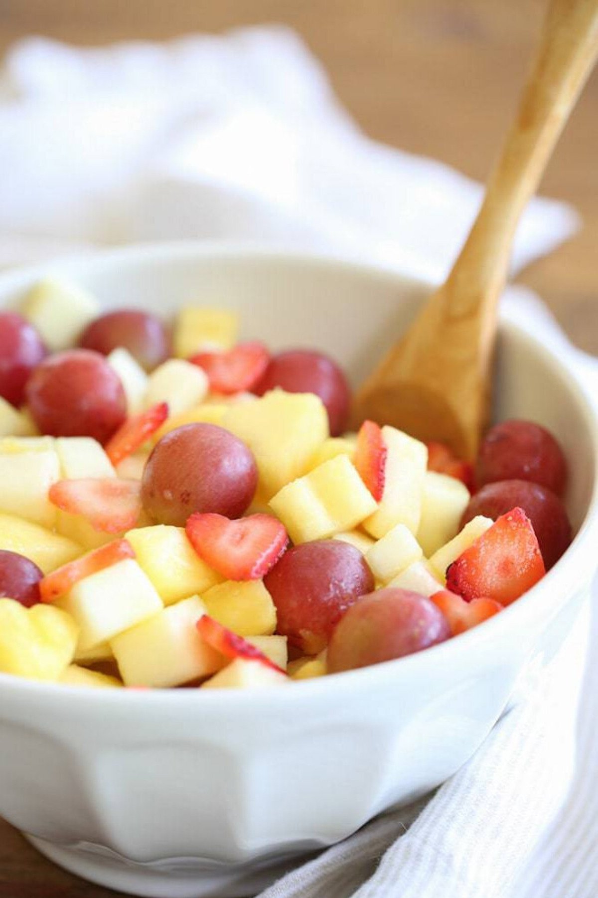 Mother's Day brunch fruit salad in a white bowl with a wooden spoon.