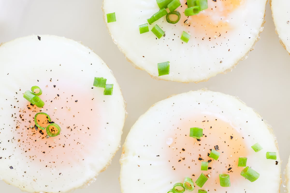 A plate of sunny side up baked muffin pan eggs garnished with herbs, pepper, and salt.