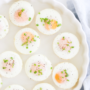 A plate of sunny side up baked muffin pan eggs garnished with herbs, pepper, and salt.