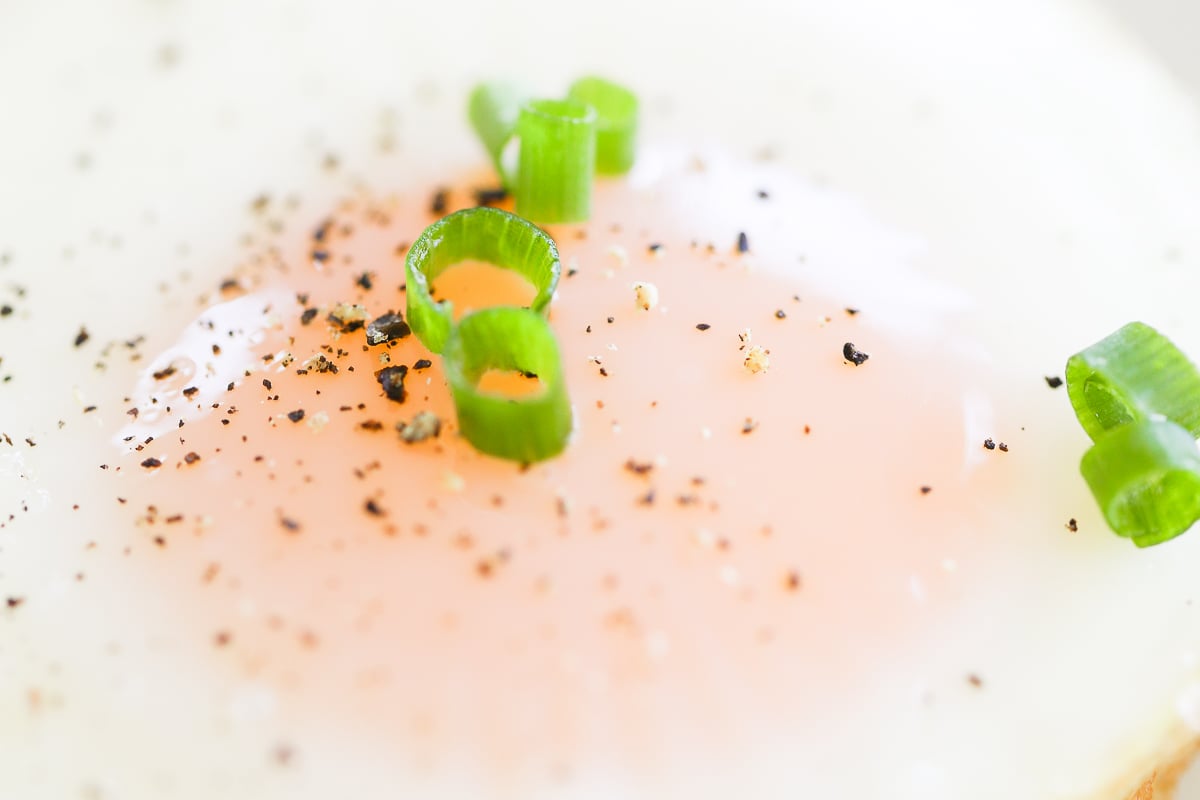 Close-up of a baked muffin pan egg garnished with green onion and black pepper.