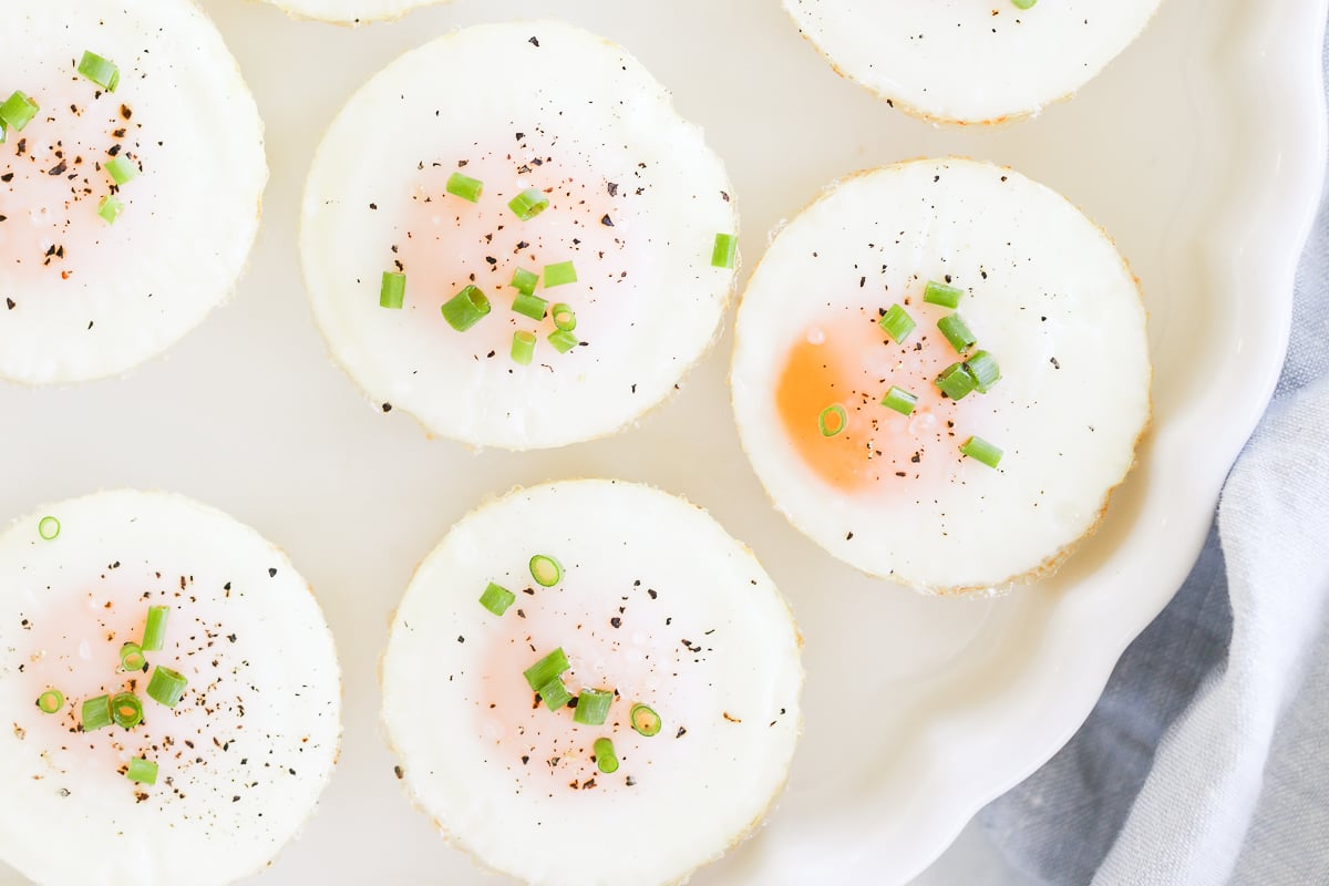 A plate of sunny side up baked muffin pan eggs garnished with herbs, pepper, and salt.