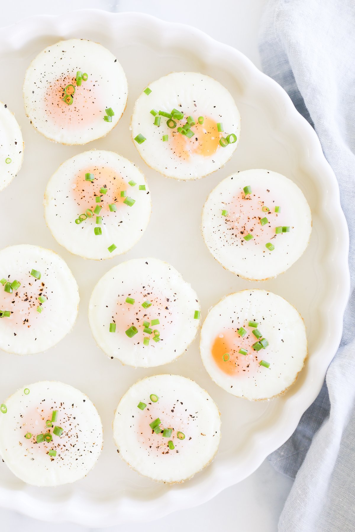 A plate of sunny side up baked muffin pan eggs garnished with herbs, pepper, and salt.