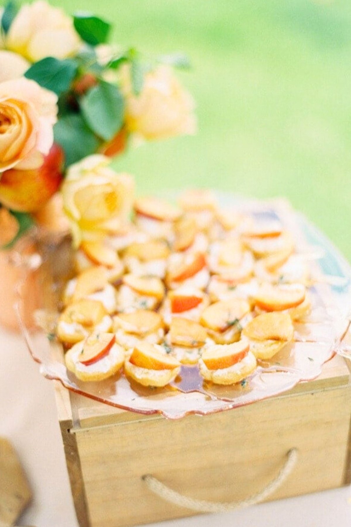 peach crostini place on a plate on top of a wooden crate in an outdoor appetizer display.