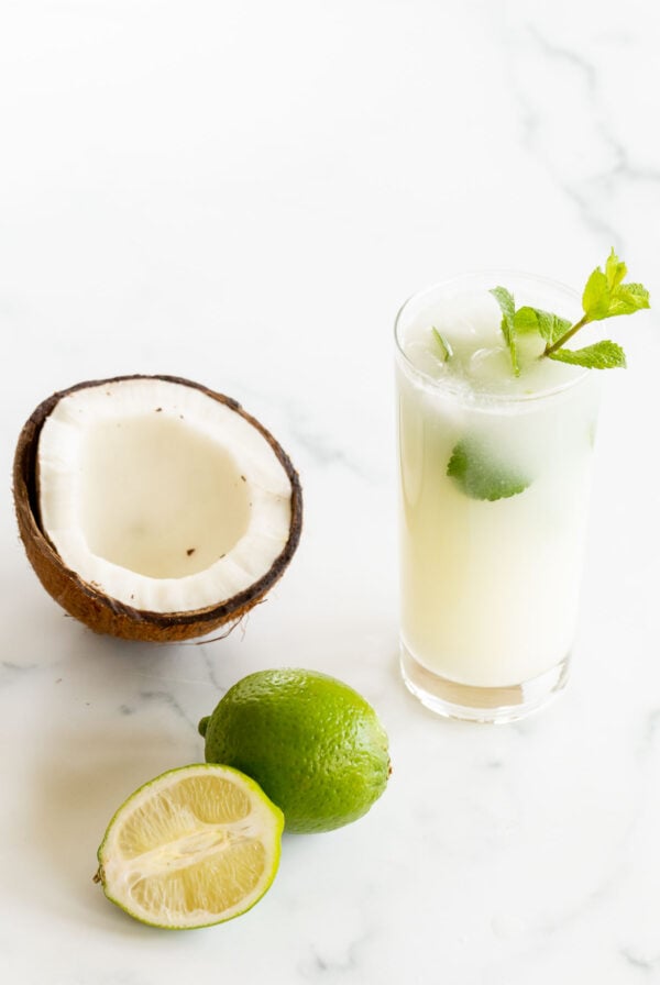 A coconut mojito recipe with a sliced coconut and limes next to it.