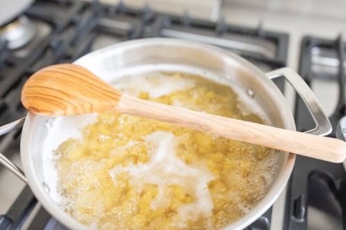 A pot of boiling chicken mushroom pasta with a wooden spoon resting on top, placed on a stove.