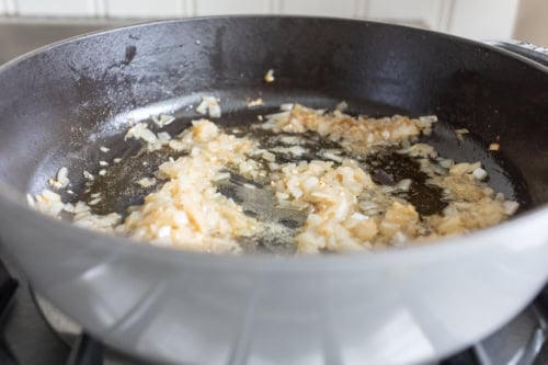 Chopped onions and mushrooms being sautéed in oil in a black frying pan on a stove.