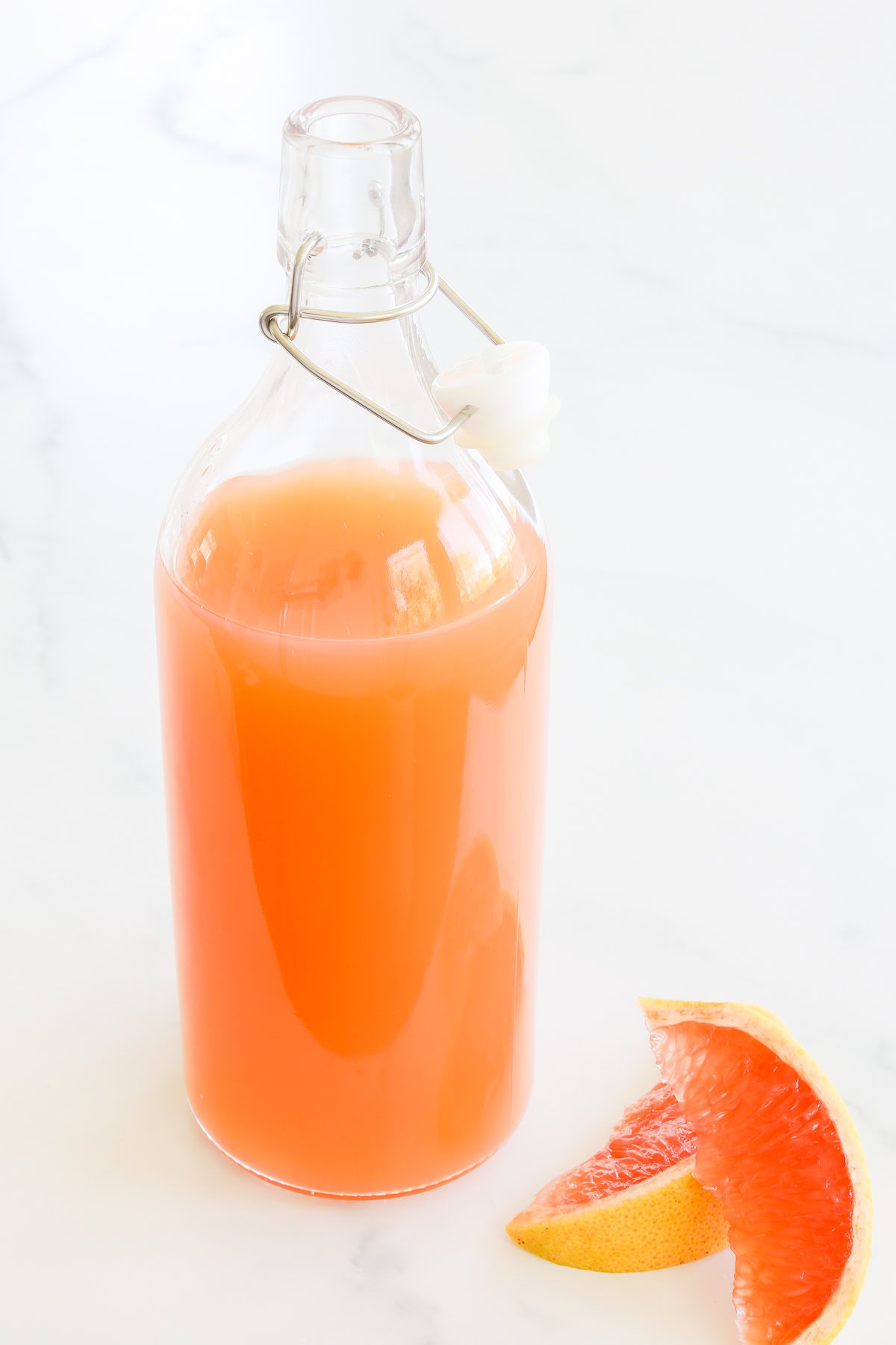 A clear glass bottle with a metal clasp containing paloma mix.