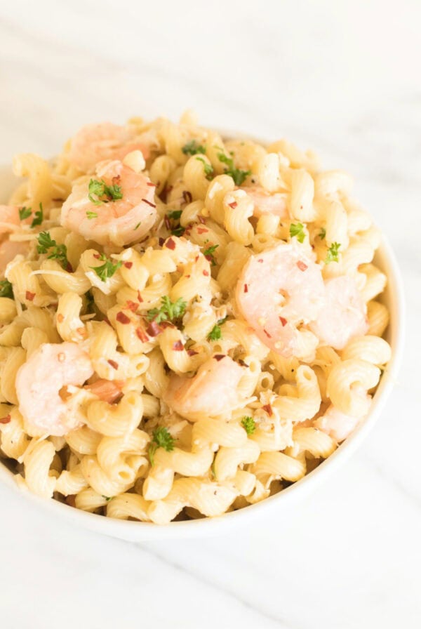 A white bowl of seafood pasta salad on a marble surface.