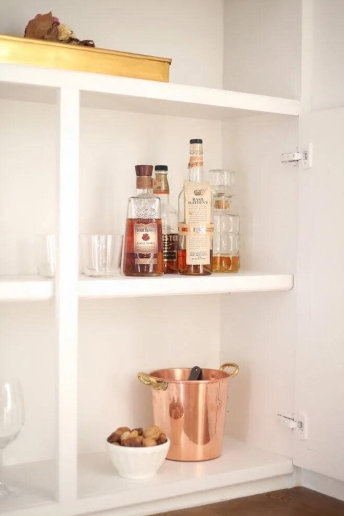 A white shelf with wine bottles, glasses, and a clock offers an elegant solution for home organization.