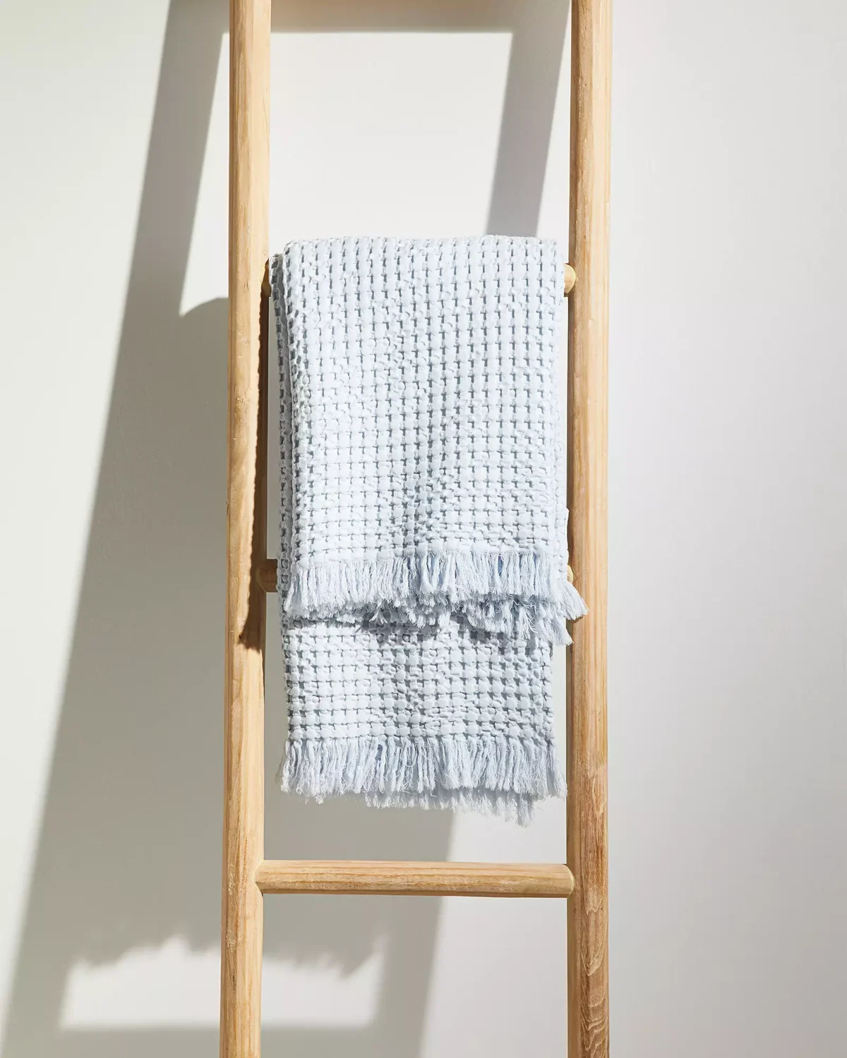 A blue sofa throw in a waffle pattern, hanging on a wooden blanket ladder.