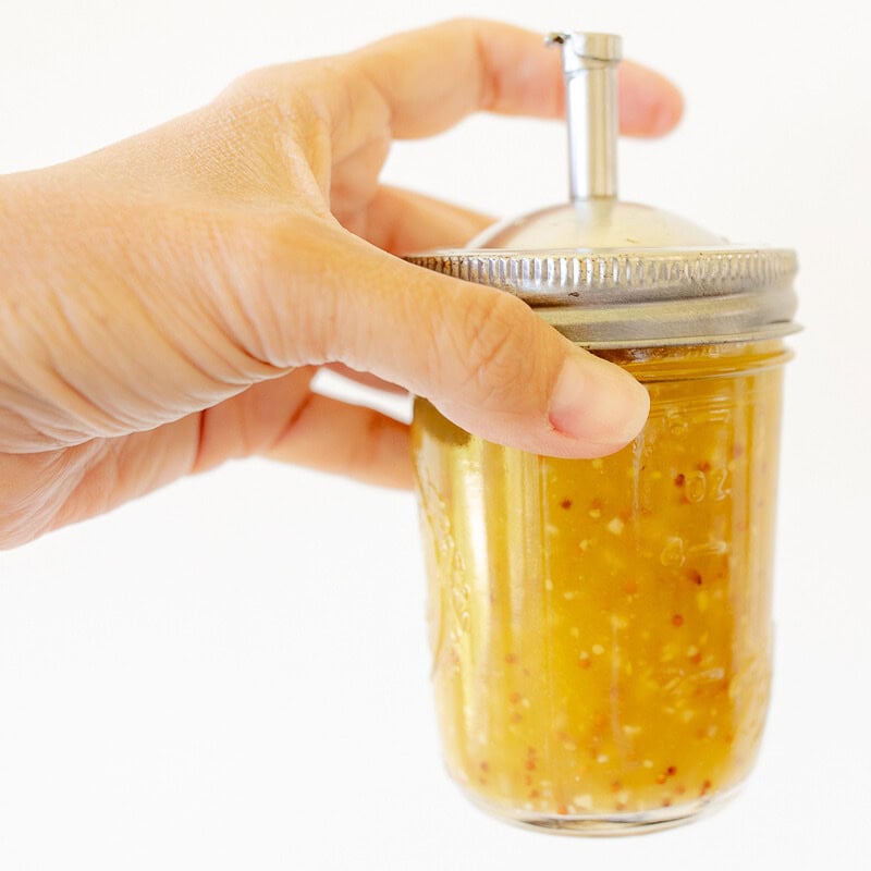 A hand holding a mason jar full of salad dressing